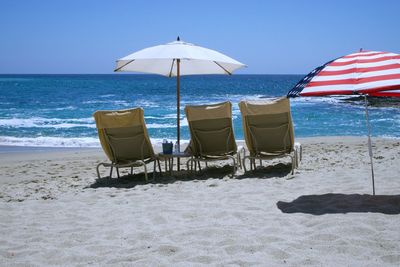 Deck chairs on beach against clear blue sky