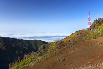 Communications tower on mountain by clouds against blue sky