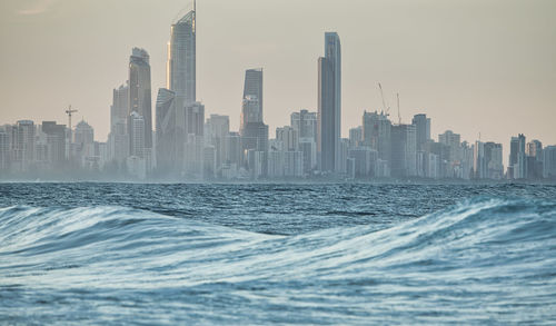 Sea by modern buildings in city against sky