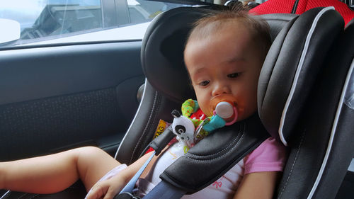Baby girl sucking pacifier while sitting in car