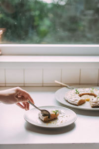 Cropped hand having dessert at table by window