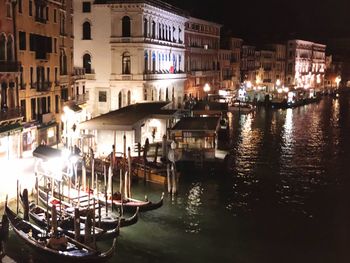 Boats moored in canal by buildings in city at night