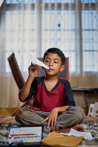 Contemplating boy looking at paper airplane while sitting on bed