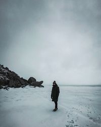 Man standing on frozen sea against cloudy sky