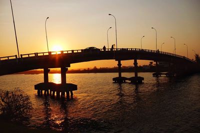 Silhouette bridge over river against sky during sunset