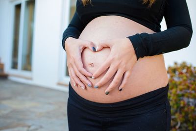 Midsection of pregnant woman making heart shape on her belly