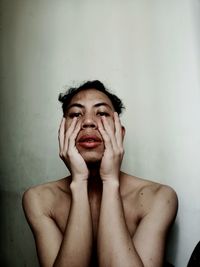 Portrait of shirtless young man with head in hands against wall