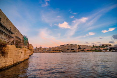 Buildings by river against cloudy sky