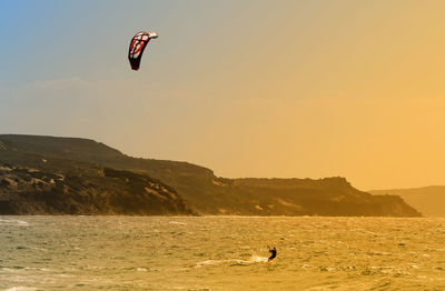 Person paragliding over sea against sky during sunset