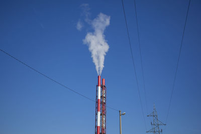 Low angle view of smoke emitting from chimney against clear blue sky