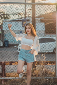 Portrait of young woman standing by chainlink fence