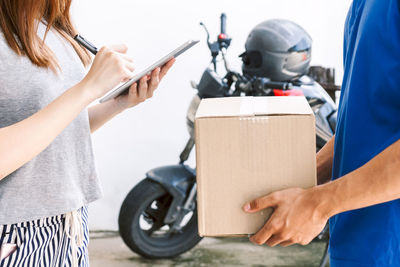 Midsection of woman signing while receiving cardboard box from delivery person outdoors
