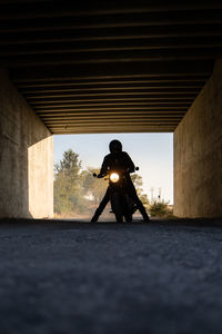 Silhouette of unrecognizable racer sitting on motorbike with switched on headlamps in tunnel