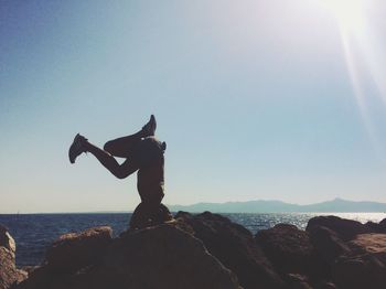 Man doing headstand on rock by sea against clear sky