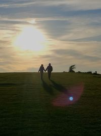 Two men playing on golf course against sky during sunset