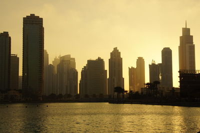 Sea by cityscape against sky during sunset