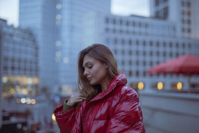 Close-up of thoughtful young woman wearing warm clothing in city during sunset