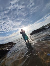 Man on rock at beach against sky