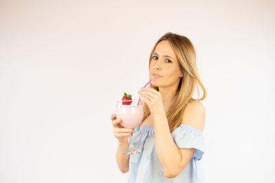 Portrait of a beautiful young woman drinking glass against white background