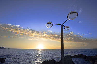 Street light by sea against sky during sunset