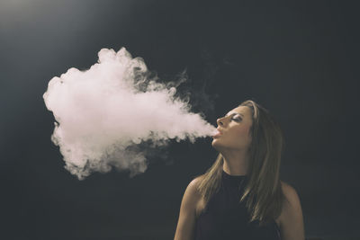 Close-up of young woman smoking over black background