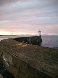Lighthouse by sea against sky during sunset