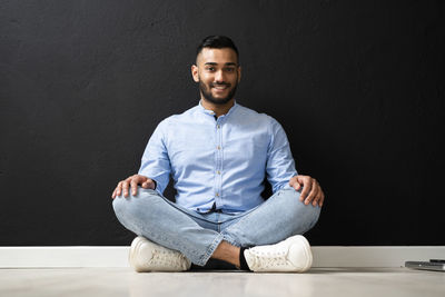 Portrait of young man sitting against wall