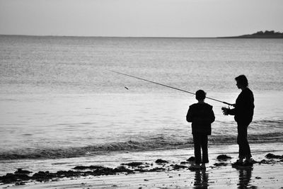 Silhouette father with son fishing at sea shore
