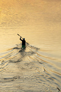 Rear view of man sailing in sea during sunset