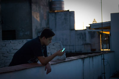 Young man using smart phone while leaning on retaining wall