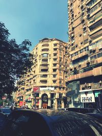 Cars on city street by modern buildings against sky