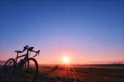 Bicycle on field against clear sky during sunset