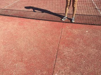 Low section of woman standing by net on brown tennis court