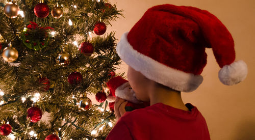Rear view of boy wearing santa hat against christmas tree