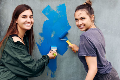 Portrait of smiling young woman standing against wall