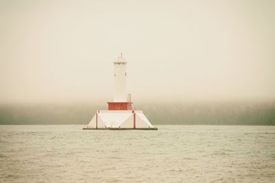 Lighthouse by sea against clear sky