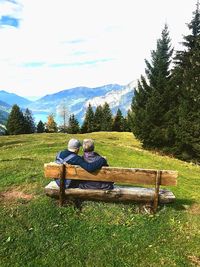 Men sitting on bench by plants against sky