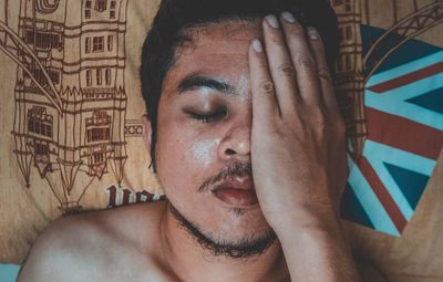 High angle view of man covering face while sleeping on bed at home