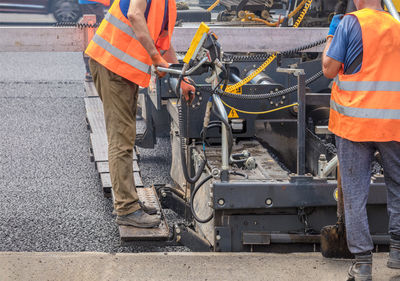 Road specialists in orange vests are laying fresh asphalt on the carriageway.