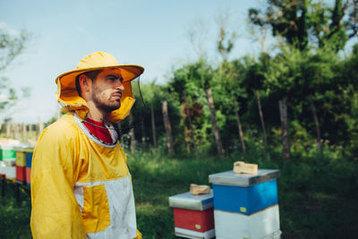 Side view of beekeeper standing by beehives on land