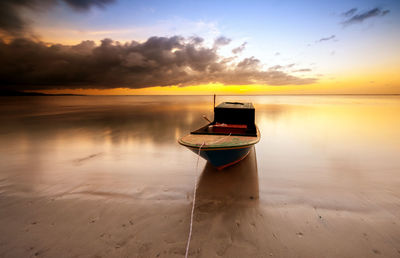 Boat moored on shore at beach against sky during sunset
