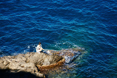 High angle view of young woman sitting on rock by sea