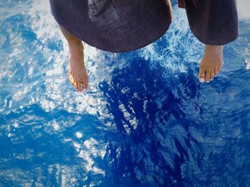 Low section of woman dangling feet over blue sea while sitting in ship