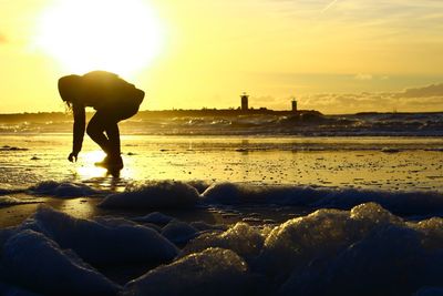 Silhouette on beach against sky during sunset