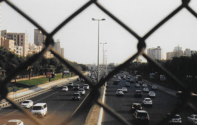Cars on street in city seen through chainlink fence