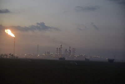 Fire emitting from smoke stack at industrial site against sky