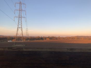 Electricity pylon on land against sky during sunset