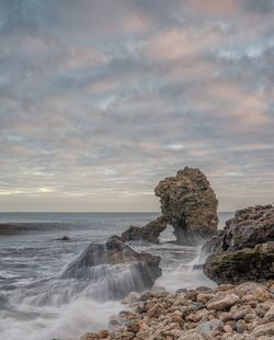 Rock formation on beach against sky during sunset