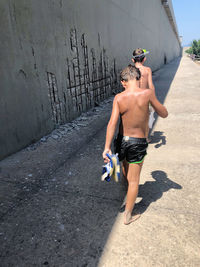 Rear view of shirtless man standing against wall