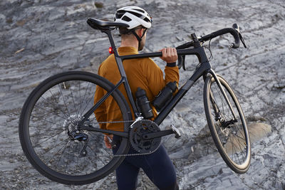 Young cyclist carrying bicycle standing on rock